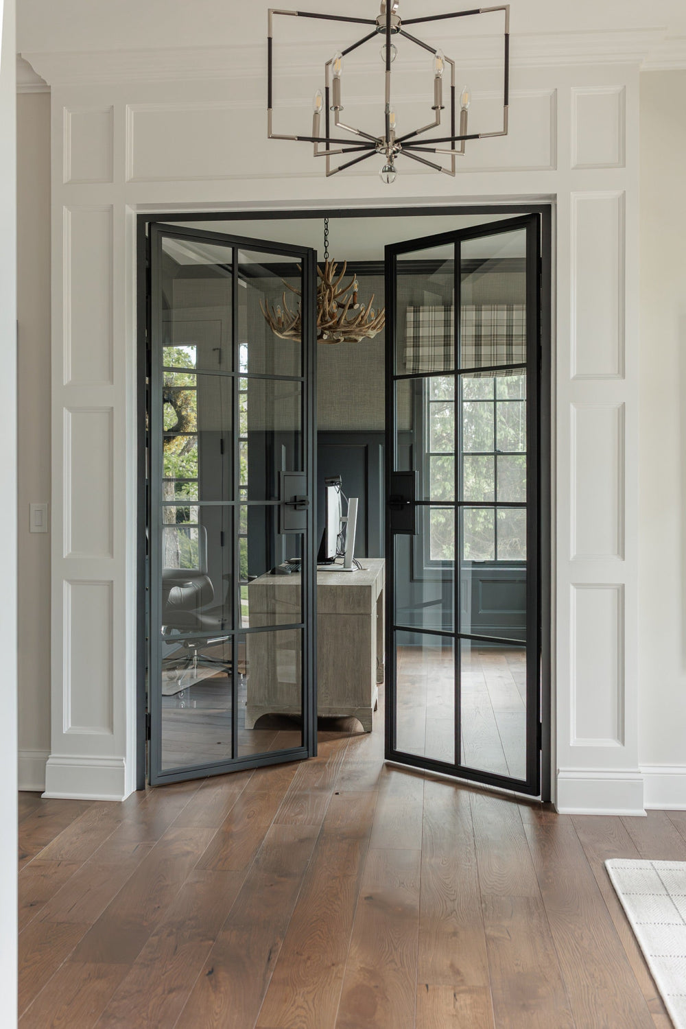 Both matte black 8 Lite steel French doors open to the home office, wood floor, chandelier above the doorway, Ohio